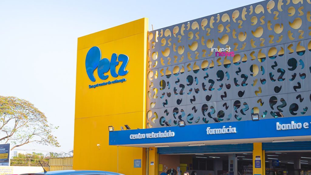 Fachada da loja Petz em dia ensolarado, com grande painel amarelo e cinza decorado, e toldo azul na entrada.