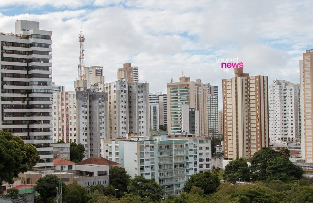 Vista aérea de uma cidade com inúmeros arranha-céus, vegetação esparsa e céu cinzento.