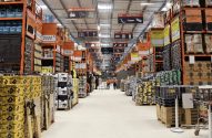 Ampla loja de materiais de construção com longos corredores repletos de produtos e funcionários trabalhando.