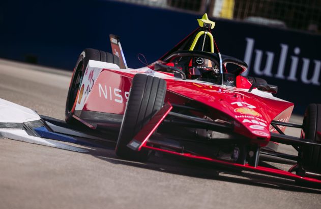 Carro Nissan de Fórmula E, vermelho e branco, fazendo curva em pista de corrida.
