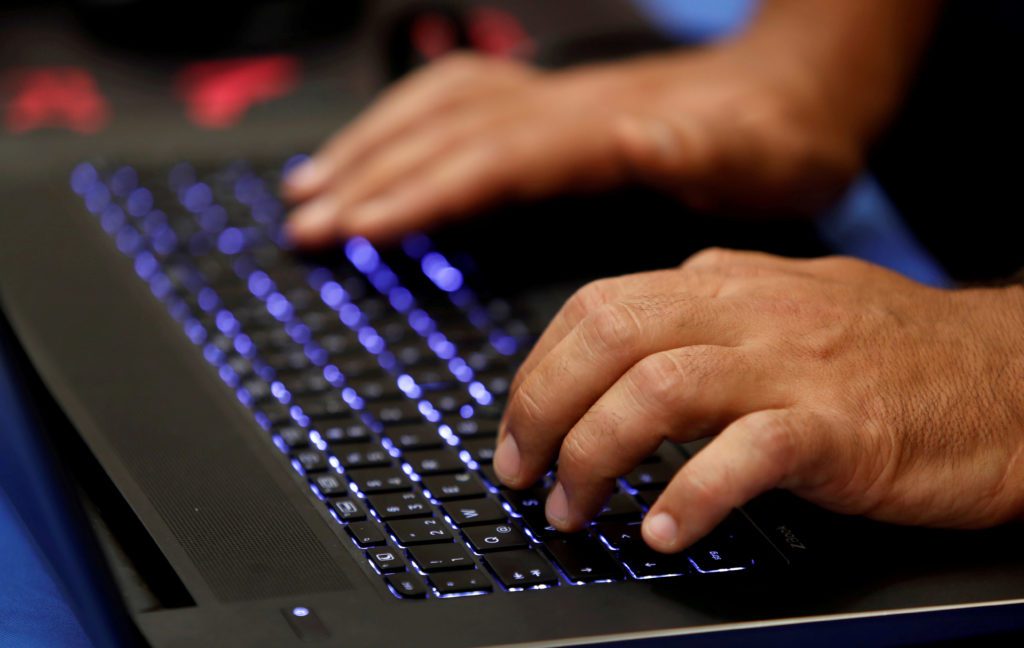 Mãos digitando em um teclado de notebook retroiluminado em azul.