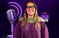 Mulher sorrindo, de óculos, posa ao lado de microfone vintage roxo, com logo "Invest News Talk IN$" neon.