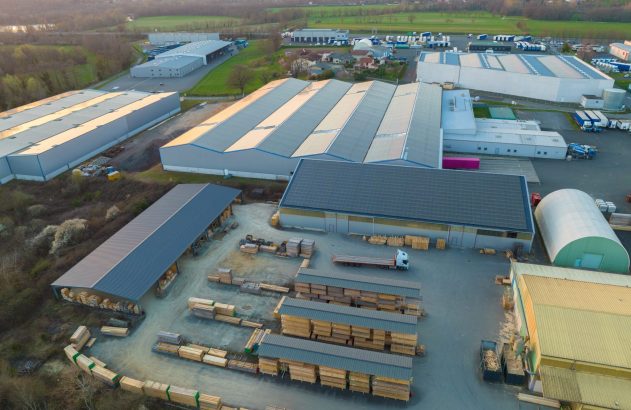 Complexo industrial com galpões, painéis solares e vasto estoque de madeira. Vista aérea.