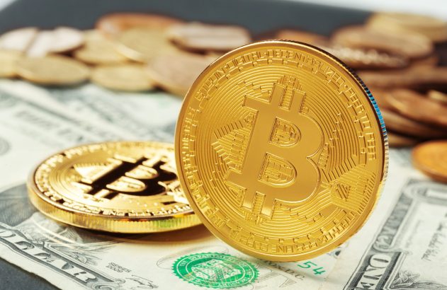 Duas moedas Bitcoin douradas sobre notas de dólar, uma delas em pé.
