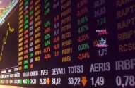 Tela digital de bolsa de valores com cotações de ações em alta (verde) e baixa (vermelho).
