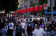 Multidão de pessoas caminhando em rua decorada com bandeiras da China; muitos usam máscaras.