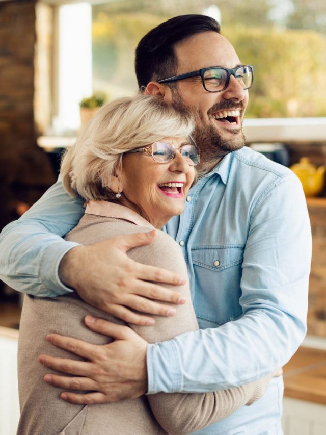 Cheerful man and his mature mother embracing in the kitchen.