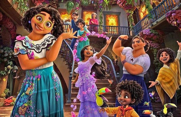 Personagens de Encanto, com Mirabel à frente, posam sorrindo na colorida casa Madrigal, cheia de flores.