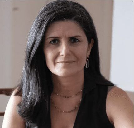 Retrato de mulher com cabelos escuros e sorriso leve, olhando para a câmera.