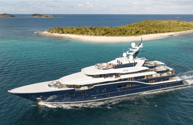 Superiate azul escuro navegando em águas turquesa cristalinas perto de ilhas tropicais com praias de areia branca.