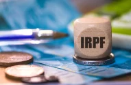 um peso de papel com as siglas IRPF em cima de uma moeda e de cédulas de real