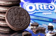 Pilha de Oreos, um em destaque, e pedaços em superfície refletiva. Pacote Oreo desfocado ao fundo.
