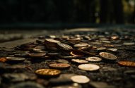 Moedas espalhadas e empilhadas sobre um chão escuro, iluminadas por luz solar