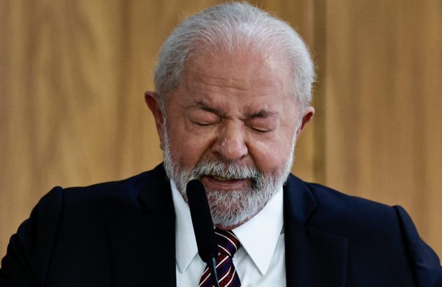 Presidente Lula com olhos fechados e feição emocionada, diante de um microfone.