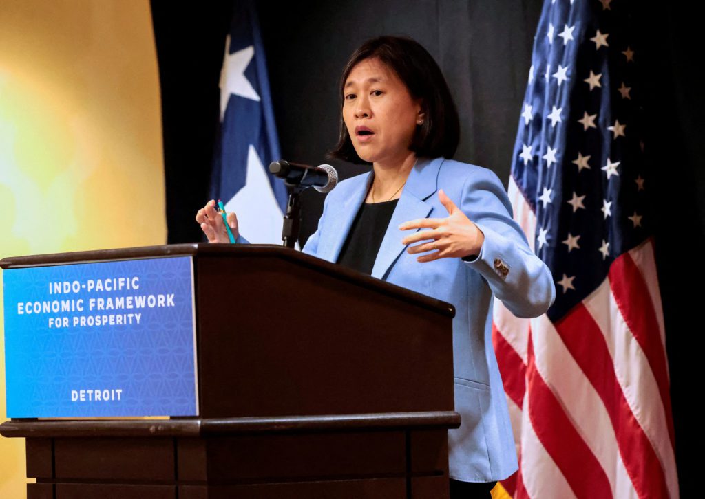 Mulher discursa em pódio gesticulando. Atrás, bandeiras dos EUA e banner 'Indo-Pacific Economic Framework'.