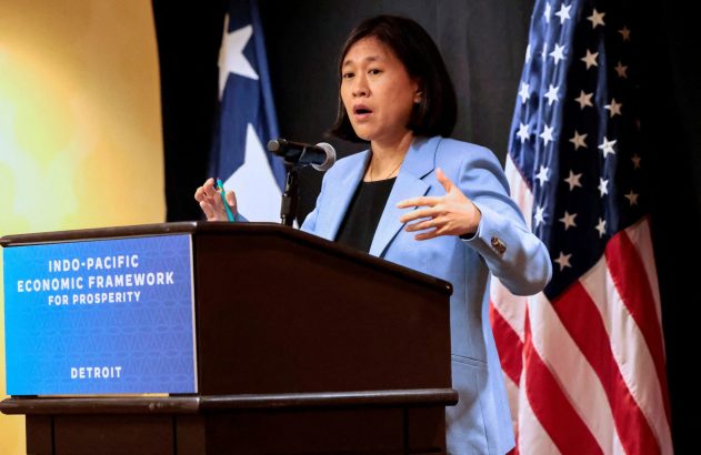 Mulher discursa em pódio gesticulando. Atrás, bandeiras dos EUA e banner 'Indo-Pacific Economic Framework'.