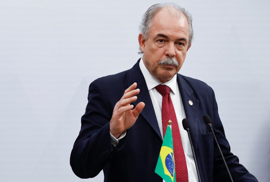 Homem de terno, gravata com bandeira do Brasil e bigode grisalho, gesticula ao falar.