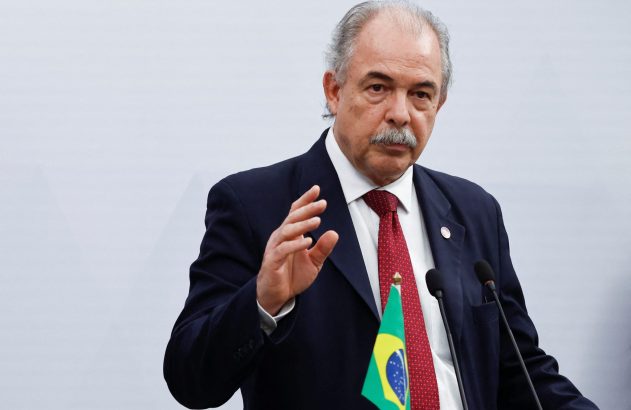 Homem de terno, gravata com bandeira do Brasil e bigode grisalho, gesticula ao falar.