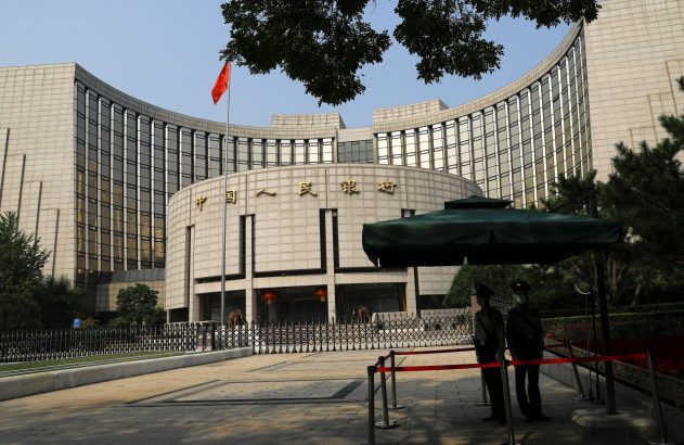 Edifício do Banco Popular da China com bandeira chinesa no alto e dois guardas uniformizados na frente.