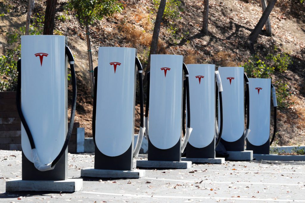 Fileira de carregadores Tesla brancos com o logotipo vermelho, em estação de recarga para veículos elétricos.