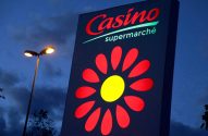Letreiro iluminado da "Casino supermarché" com logo de flor vermelha e amarela, à noite, com poste de luz.