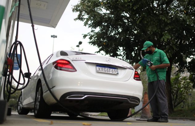 Frentista abastece carro branco Mercedes-Benz em posto de gasolina.