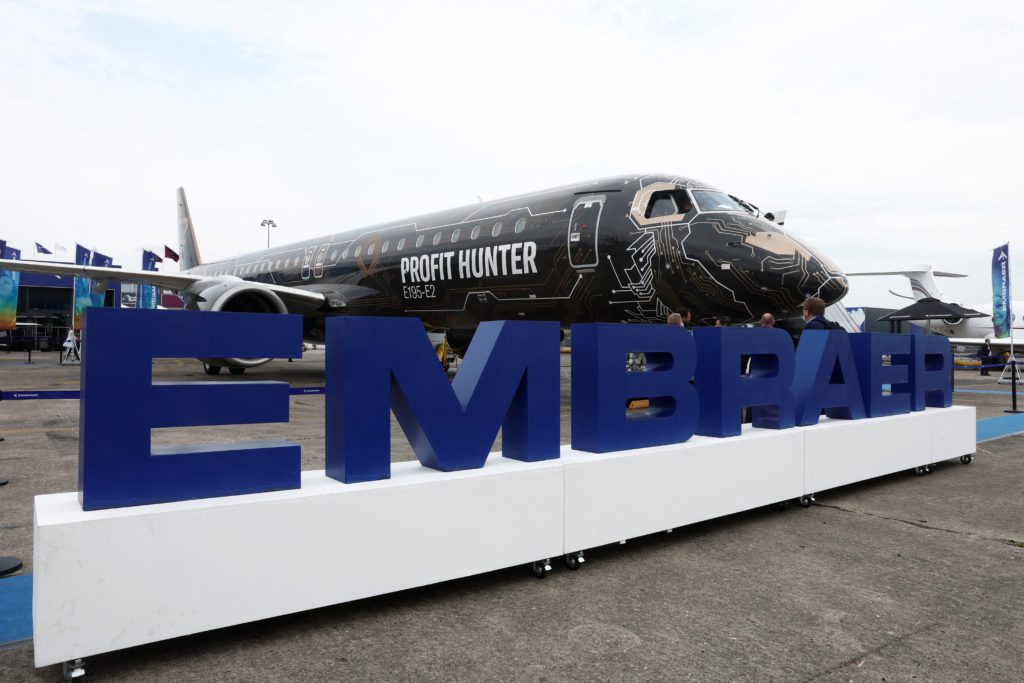 Aeronave Embraer preta "Profit Hunter" com pintura de circuito e letreiro "EMBRAER" azul em evento ao ar livre.