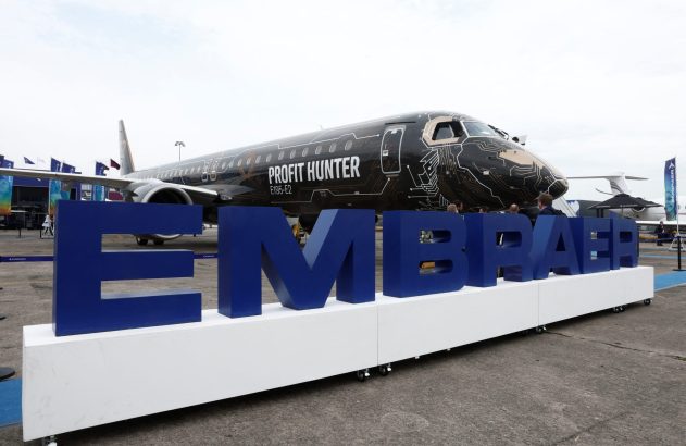Aeronave Embraer preta "Profit Hunter" com pintura de circuito e letreiro "EMBRAER" azul em evento ao ar livre.