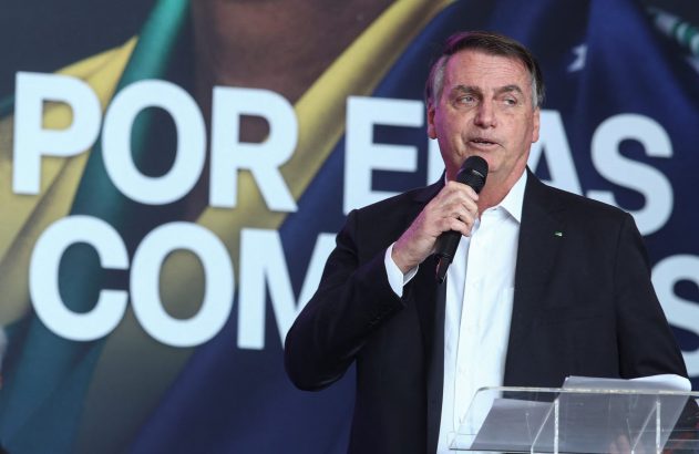 Jair Bolsonaro, de terno, fala em microfone num púlpito, com banner ao fundo.