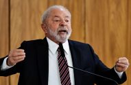 Lula, de barba branca e terno, discursa em microfone, gesticulando com as mãos. Fundo de madeira.