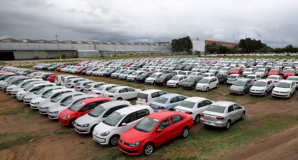 Centenas de carros novos estacionados em um grande pátio de fábrica sob céu nublado.