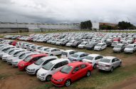 Centenas de carros novos estacionados em um grande pátio de fábrica sob céu nublado.