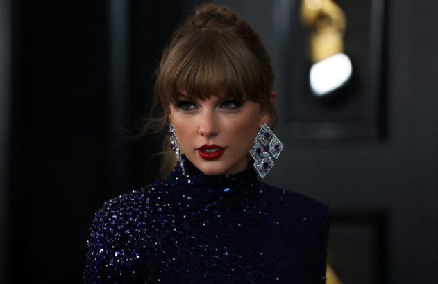 Taylor Swift em vestido azul brilhante com lantejoulas, cabelo preso e franja, usando brincos grandes, olhando para o lado.