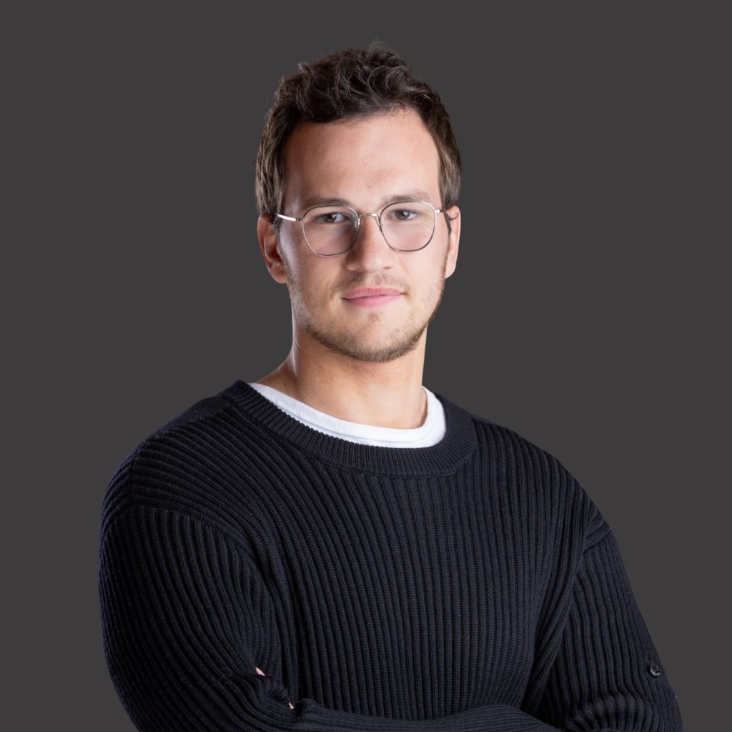 Retrato de homem com óculos e suéter preto, olhando à frente.
