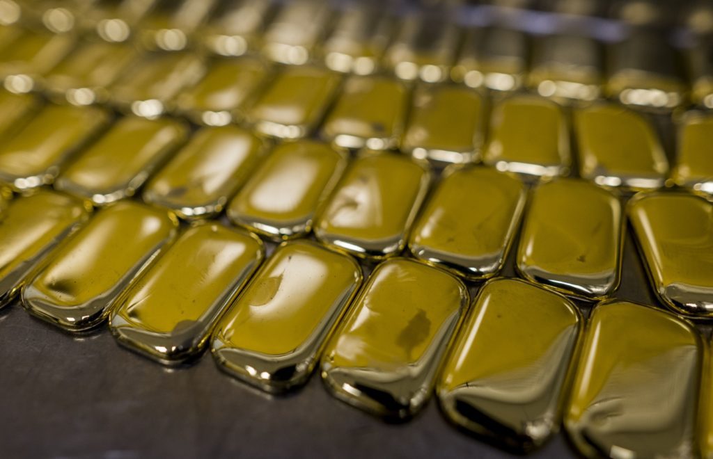 Muitas barras de ouro retangulares e brilhantes em fileiras sobre uma superfície escura.