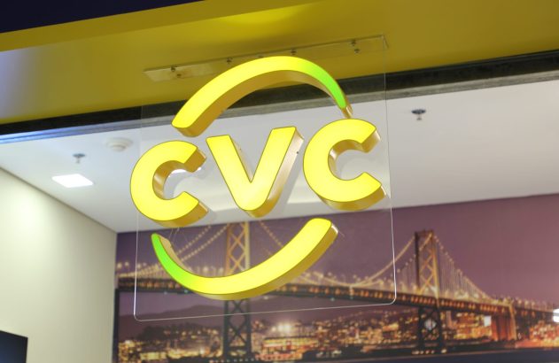 Letreiro CVC amarelo iluminado com detalhes verdes, suspenso à frente de um mural de ponte e cidade noturna.