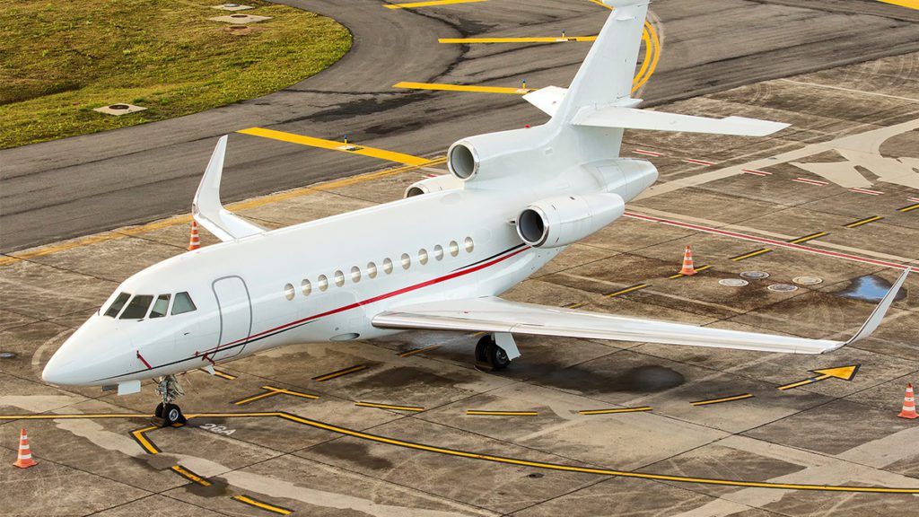Jato particular branco estacionado em pátio de aeroporto. Visível de cima, com marcações amarelas e cones.