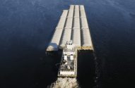 Vista aérea de um empurrador empurrando um comboio de grandes barcaças carregadas em um rio.