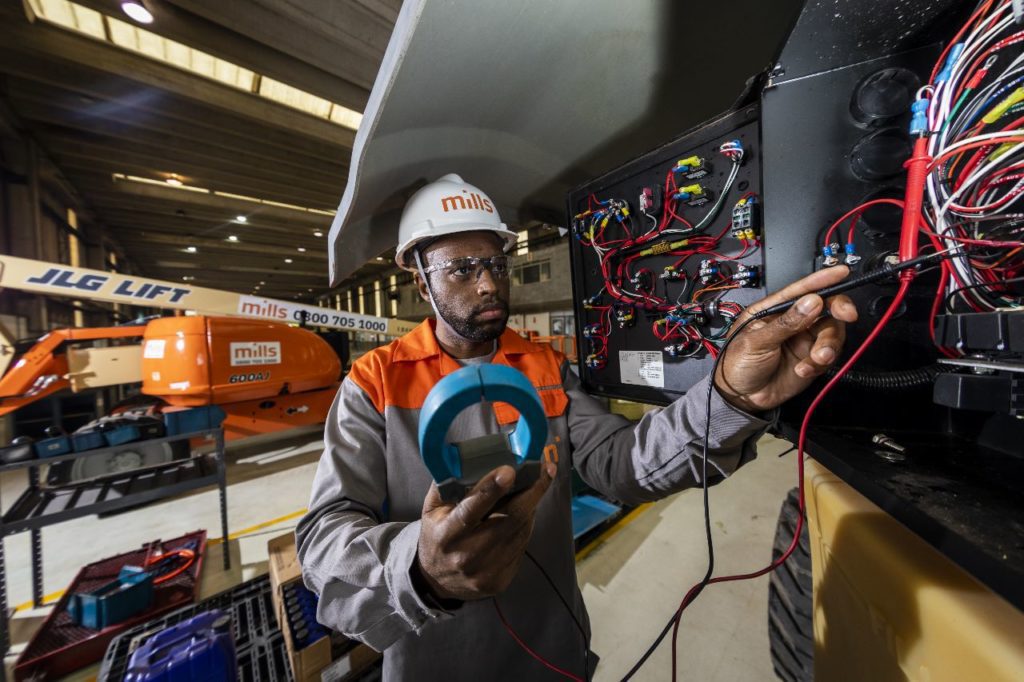 Eletricista inspeciona painel elétrico com multímetro em ambiente industrial.