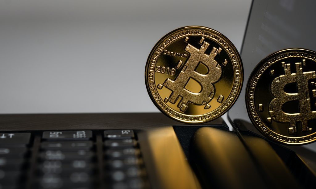 Duas moedas douradas de Bitcoin sobre um laptop, uma com o ano 2018 em destaque.