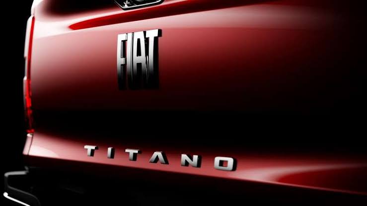 Traseira de picape Fiat Titano vermelha, com logotipos cromados 'FIAT' e 'TITANO' em destaque sobre a lataria brilhante.