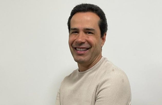 Retrato de homem sorrindo, olhando para a câmera, com camisa clara.