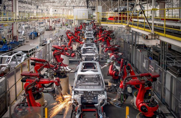 Fábrica de carros: robôs vermelhos montam carrocerias em linha de produção. Faíscas de soldagem em primeiro plano.