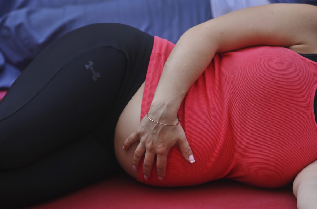Pessoa grávida deitada de lado, mão sobre a barriga, vestindo top rosa e legging preta.