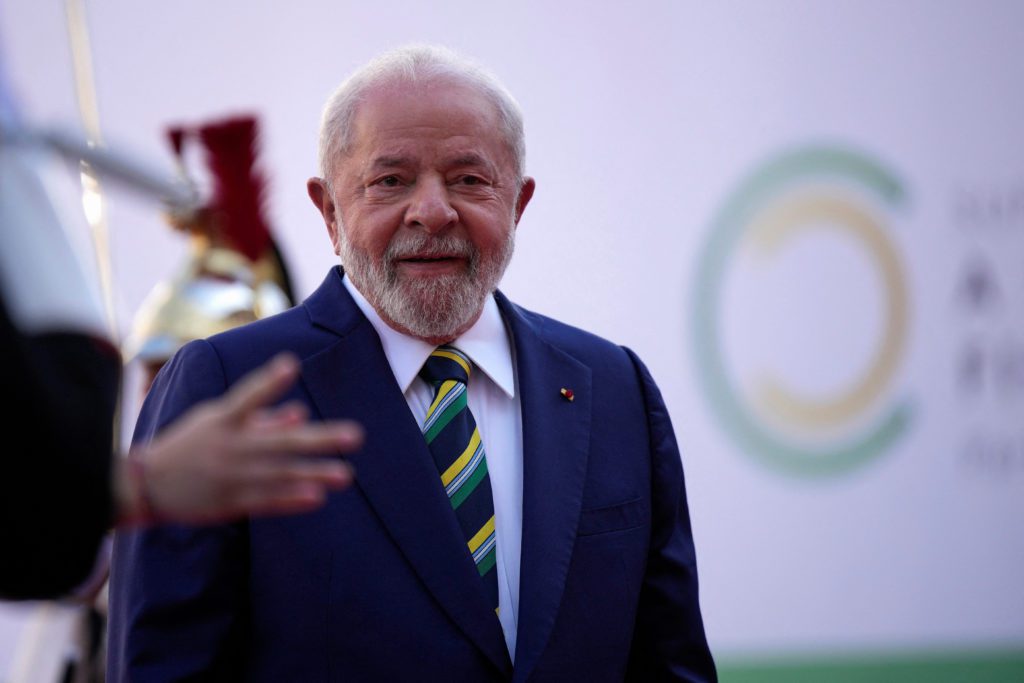 Presidente Lula sorrindo, gesticulando, em terno e gravata com cores do Brasil.