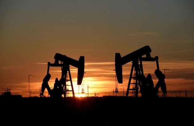 Dois cavalos de pau bombeando petróleo em silhueta ao pôr do sol.