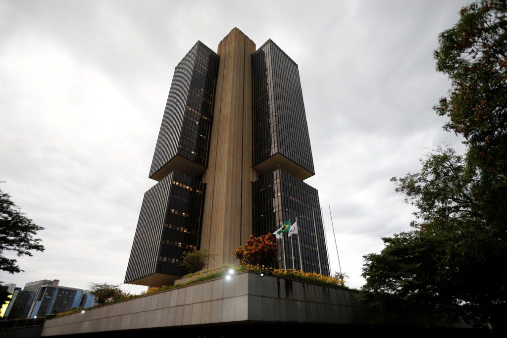Edifício alto com quatro blocos de vidro escuro e núcleo de concreto exposto, bandeira do Brasil na base.