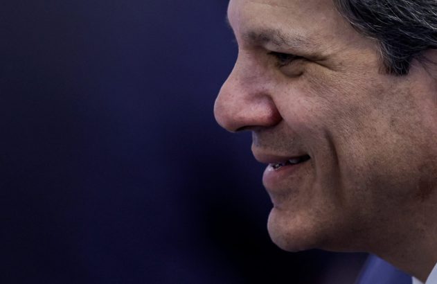 Um homem sorrindo de perfil, com cabelos grisalhos, olhando para a esquerda em um fundo azul escuro.