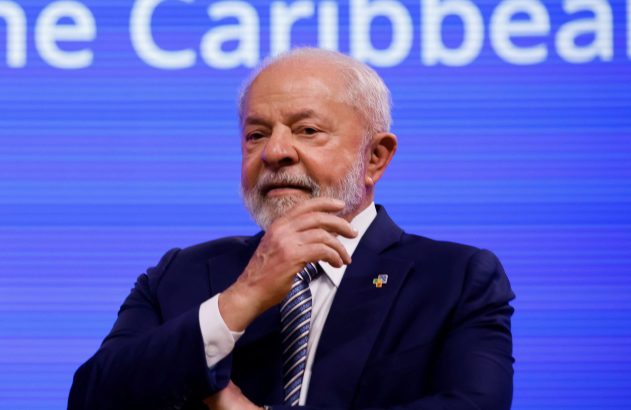 Homem de terno azul, cabelo e barba brancos, com a mão no queixo. Fundo azul com o texto 'e Caribbean'.