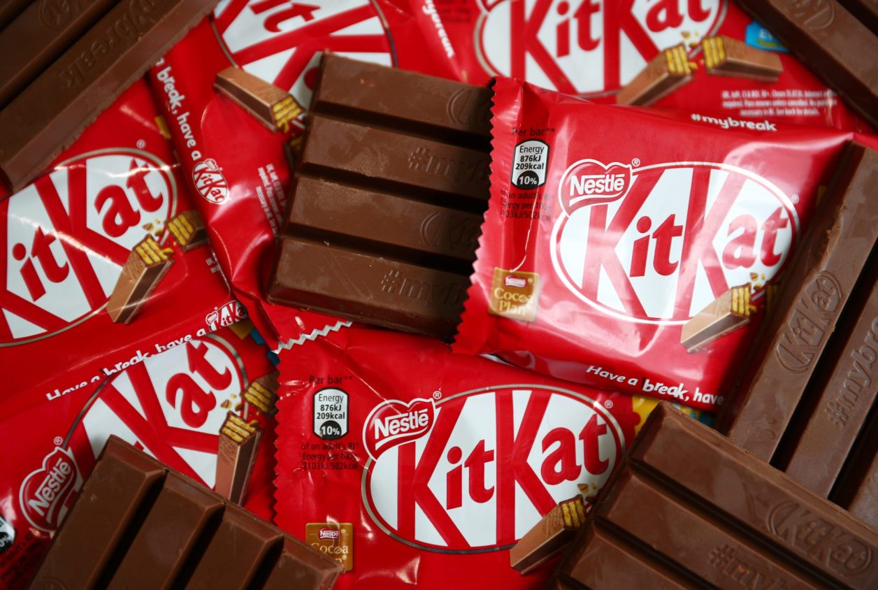 Barras de chocolate Kit Kat: algumas em embalagens vermelhas, uma aberta, e outras desembrulhadas.